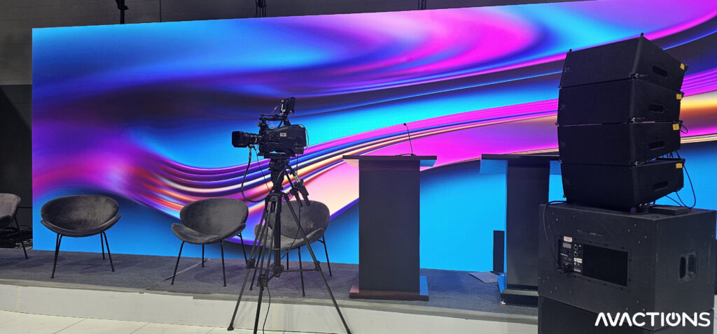 AV Actions studio showing LED wall, a broadcast camera, and line array speakers.